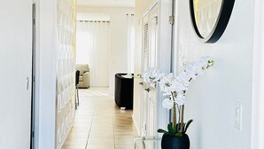 Un couloir moderne avec une console en verre, une orchidée en pot et un grand miroir mural.