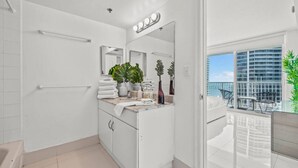 A modern bathroom with a large mirror, a sink with toiletries, and a view of a balcony with outdoor furniture. - The Club 3305 DUPLICATE · High Floor Ocean View Unit In Brickell - Parking (Miami)