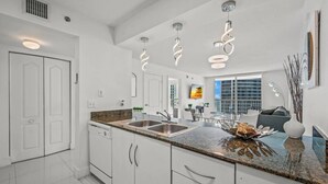 A modern kitchen with white cabinets, granite countertops, and a built-in dishwasher. There are pendant lights above the sink and a large window providing natural light. - The Club 3305 DUPLICATE · High Floor Ocean View Unit In Brickell - Parking (Miami)