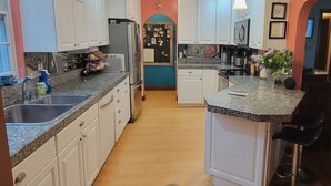 Una cocina con armarios blancos, encimera de granito, refrigerador y cafetera.