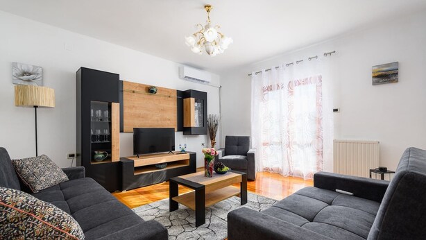 Un salon moderne avec un téléviseur à écran plat, un meuble en bois et un canapé gris.