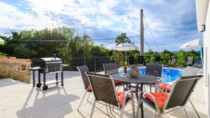 Une terrasse extérieure équipée d’un barbecue, d’une table à manger, de chaises et d’une piscine.