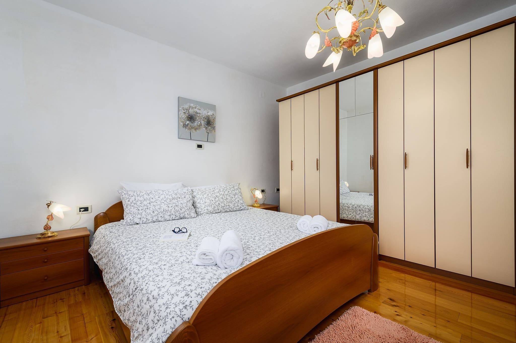 Een slaapkamer met een houten bed, nachtkastje met een lamp, een kledingkast en een schilderij aan de muur.