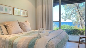 Ein Schlafzimmer mit einem großen Bett, Meerblick und einem Vorhangfenster.
