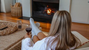 Eine Person entspannt sich auf einem Sofa, mit einem Glas Rotwein, einem Korb und einem Kamin im Hintergrund.