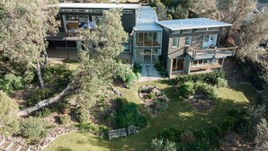 Ein modernes, zweistöckiges Haus mit einer großen Terrasse, umgeben von einem gepflegten Garten und Bäumen.