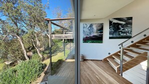Ein modernes Interieur mit einer Holztreppe, einer Glastür, die zu einem Außenbereich führt, und zwei abstrakten Gemälden an der Wand.