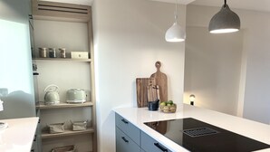 Een moderne keuken met een wit aanrecht, een zwart inductiefornuis en houten planken.