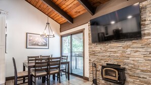 A dining area with a wooden table and chairs, a stone fireplace, and a large flat-screen TV mounted on the wall.