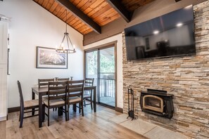 A dining area with a wooden table and chairs, a stone fireplace, and a large flat-screen TV mounted on the wall.