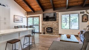 A spacious living area with a stone fireplace, a large TV mounted on the wall, and a wooden ceiling.