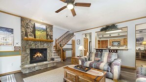 Una sala de estar con chimenea, un sofá, una mesa de centro y una escalera que lleva a una cocina.