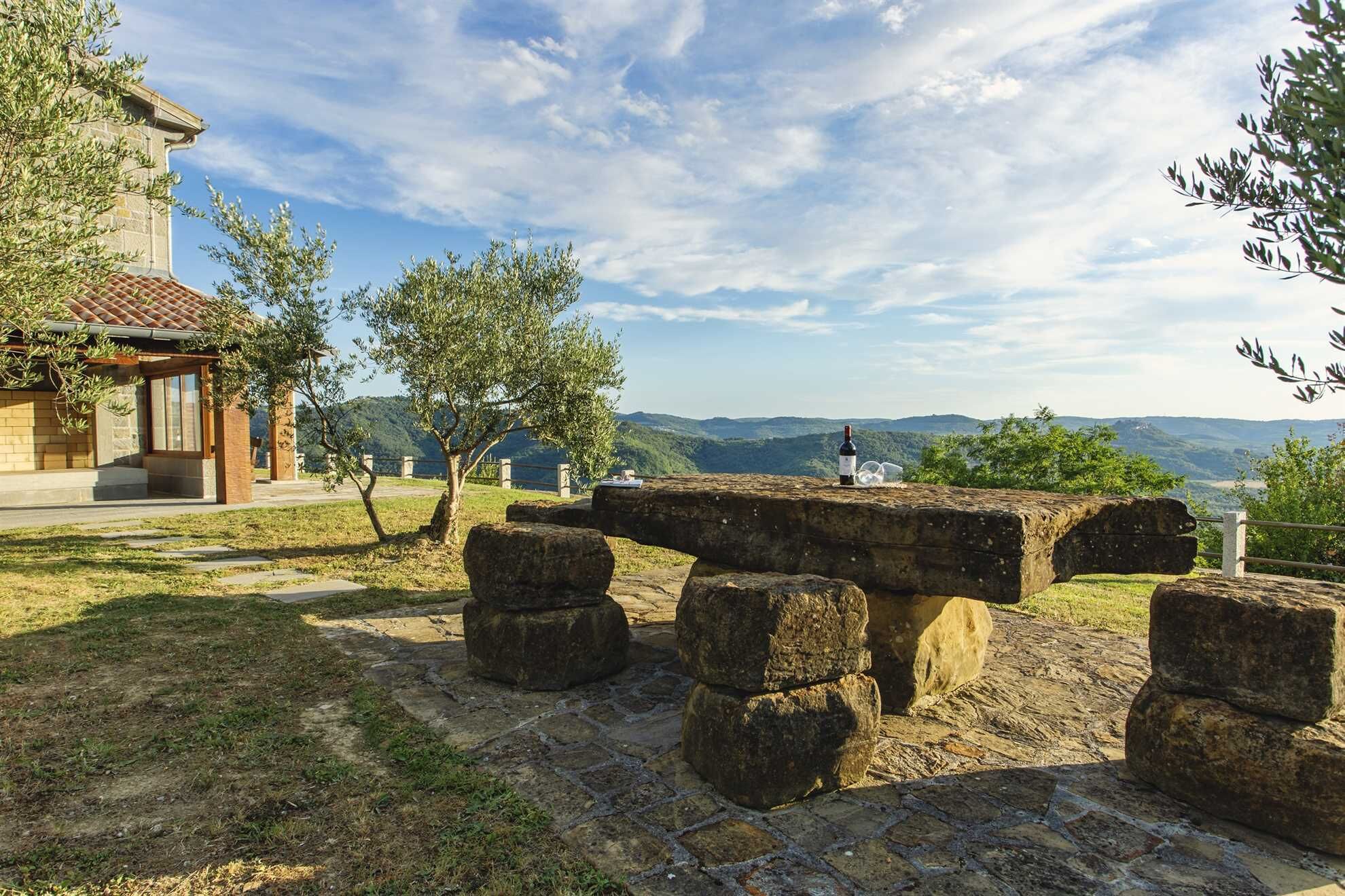 A stone structure with a stone bench, a building with a tiled roof, and a view of distant hills.