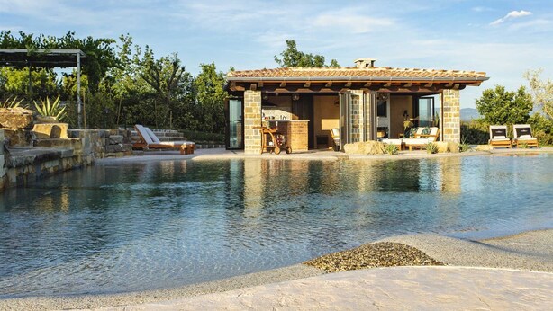 A poolside area with a stone structure, lounge chairs, and a clear view of the pool. - Luxurious Villa Bora with a large 120 m Lagoon Pool and Waterfall (Buzet)
