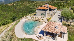 A villa with a swimming pool, stone walls, and a view of the surrounding hills. - Luxurious Villa Bora with a large 120 m Lagoon Pool and Waterfall (Buzet)