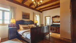 A spacious bedroom with a large bed, wooden headboard, a chandelier, and a view of the bathroom through an open door. - Luxurious Villa Bora with a large 120 m Lagoon Pool and Waterfall (Buzet)