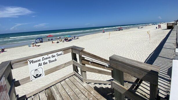 A wooden boardwalk leading to a sandy beach with a sign that reads "Please Leave the Beach At the Beach."