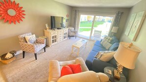A living room with a sofa, armchair, coffee table, TV stand, and a view of the outdoors.