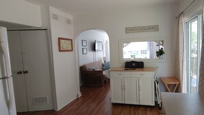 A hallway with a wooden floor, a white door, a small seating area with a chair and cushions, a white cabinet, and a window with a view of buildings outside. - Bay Beach Cottage in Crystal Beach....perfect for a quiet getaway.  (Crystal Beach)