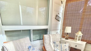 A room with two wooden-framed chairs with white cushions and blue patterns, a small white bedside table with a lamp, and a wicker basket. - Bay Beach Cottage in Crystal Beach....perfect for a quiet getaway.  (Crystal Beach)