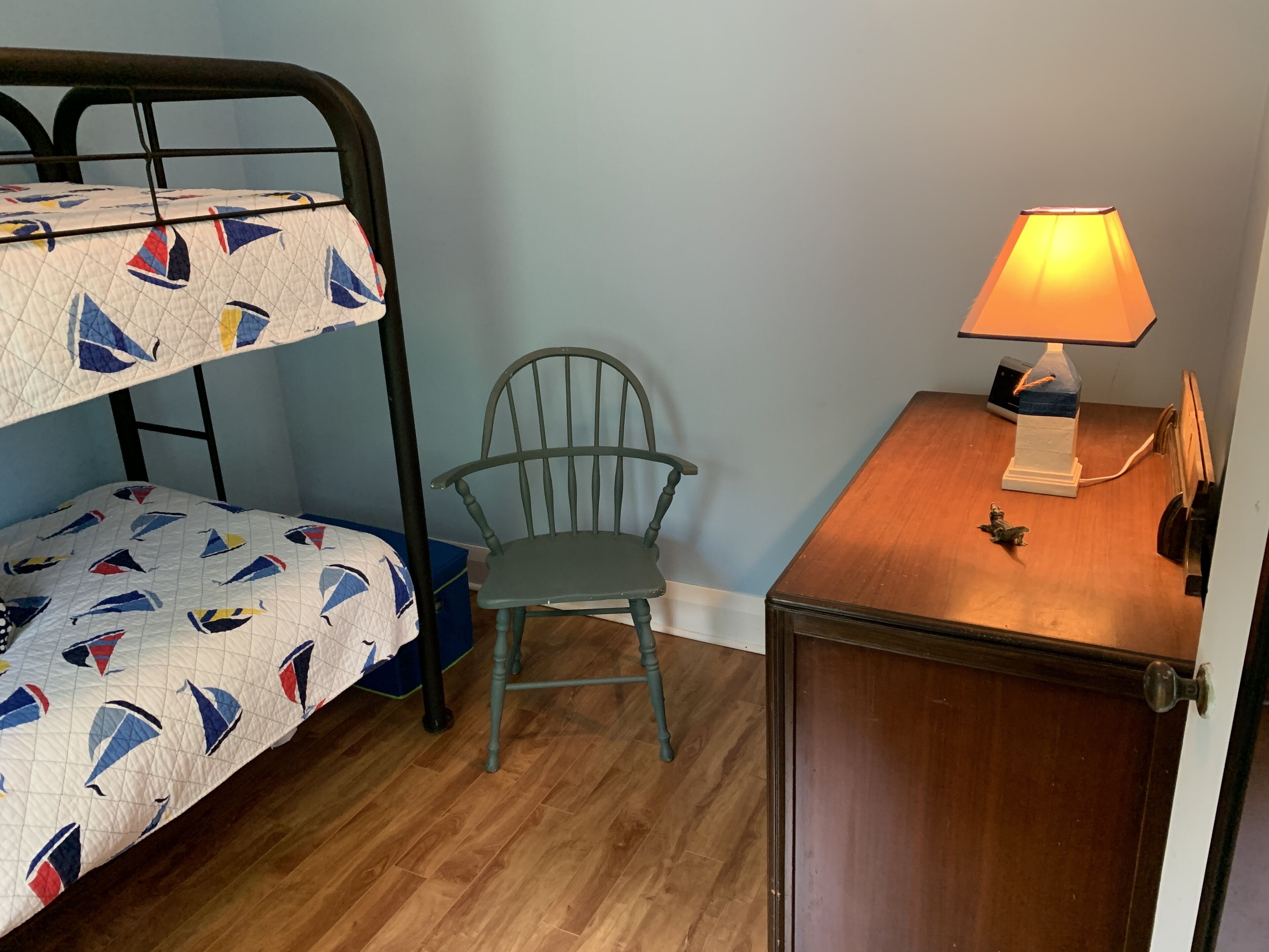 A bunk bed with a sailboat pattern, a wooden desk with a lamp, and a chair.