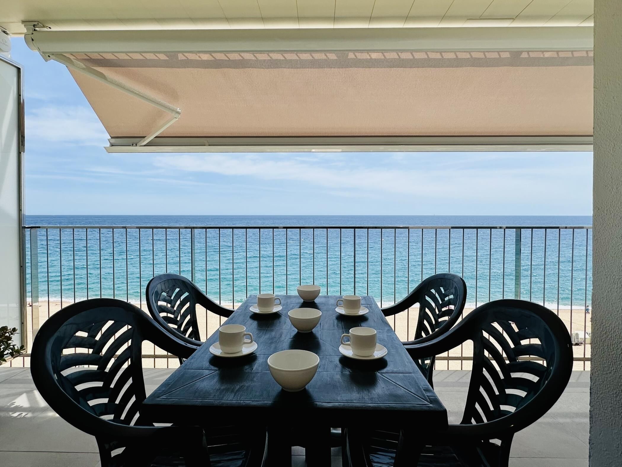 Une table entourée de chaises et agrémentée de bols, le tout installé sur un balcon donnant sur l’océan.