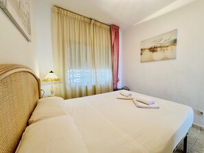 A hotel room with a bed, a lamp, a painting, and a window with curtains.