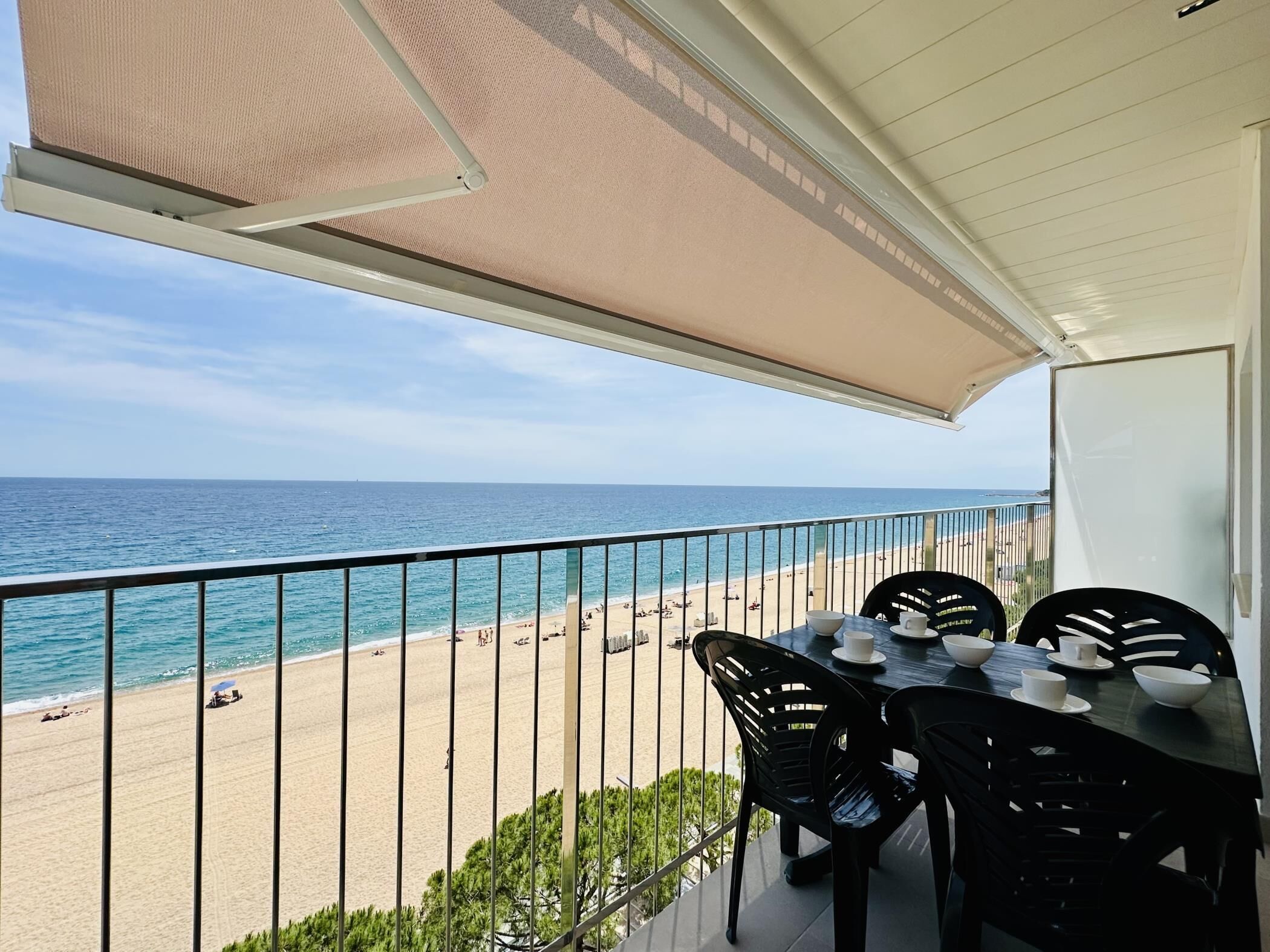 A balcony with a view of the beach and ocean, a table with chairs, and a covered area with a mesh canopy.