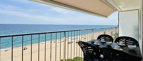 A balcony with a view of the beach and ocean, a table with chairs, and a covered area with a mesh canopy.