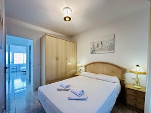 A hotel room with a bed, two bedside lamps, a wooden wardrobe, a painting on the wall, and a door leading to another room. - Sea CostaBravaSi - Beach, terrace, wifi, views (Platja d'Aro)