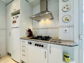 Una cucina con mobili bianchi, un fornello a gas, una cappa aspirante in acciaio inossidabile e piatti decorativi appesi al muro.