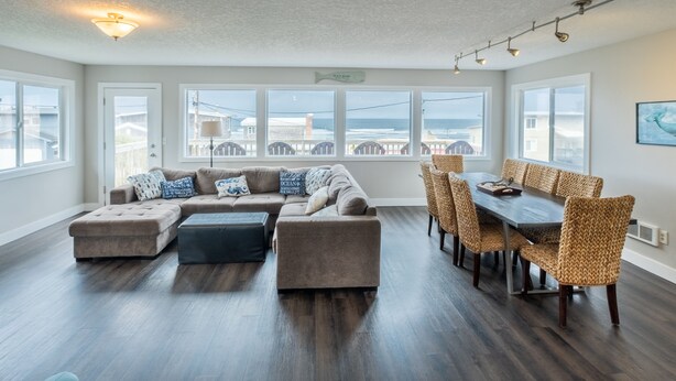 A spacious living room with a large sectional sofa, ottomans, and a dining area with wicker chairs.