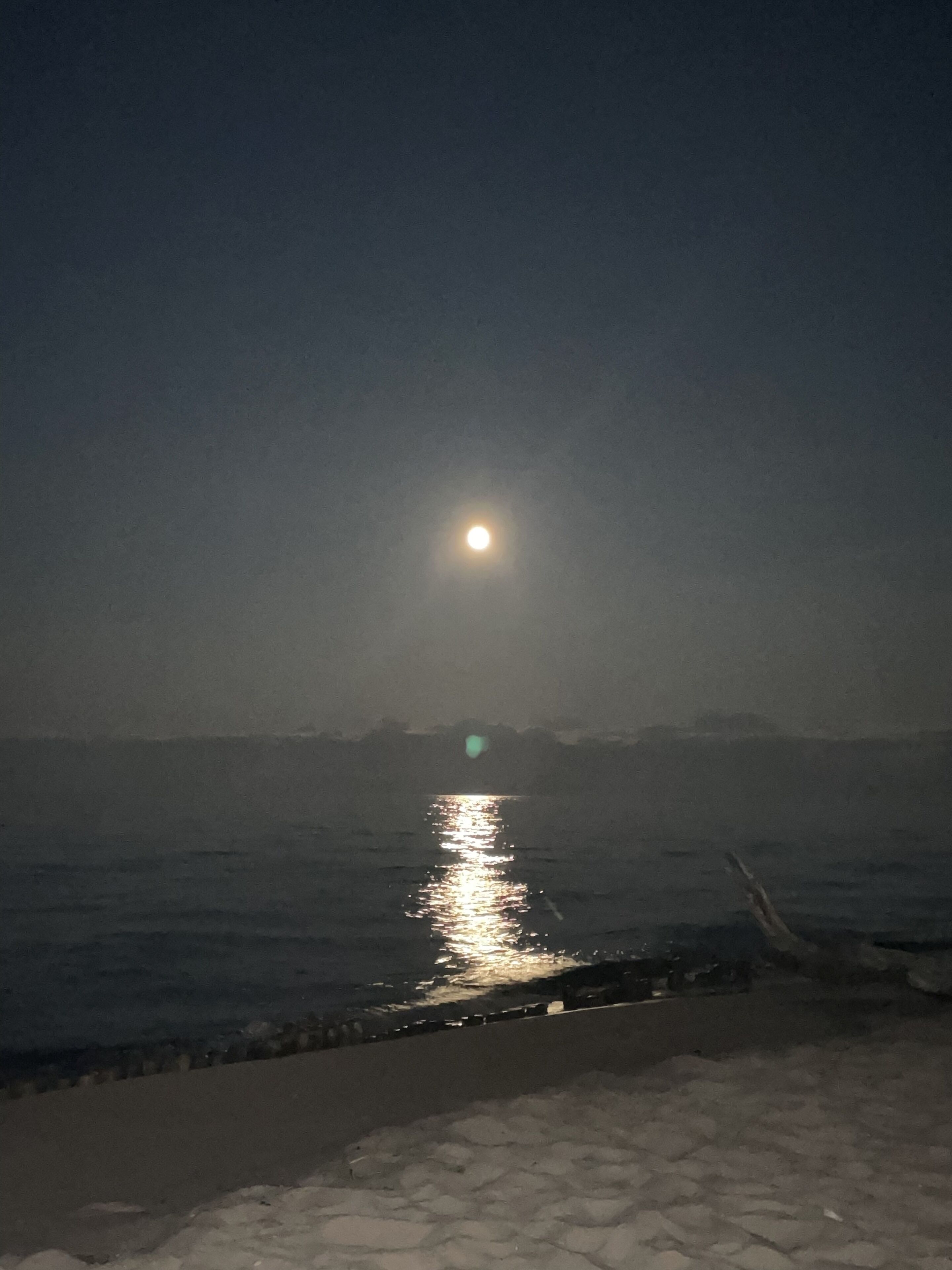 A beach at night with a visible moon reflection on the water.