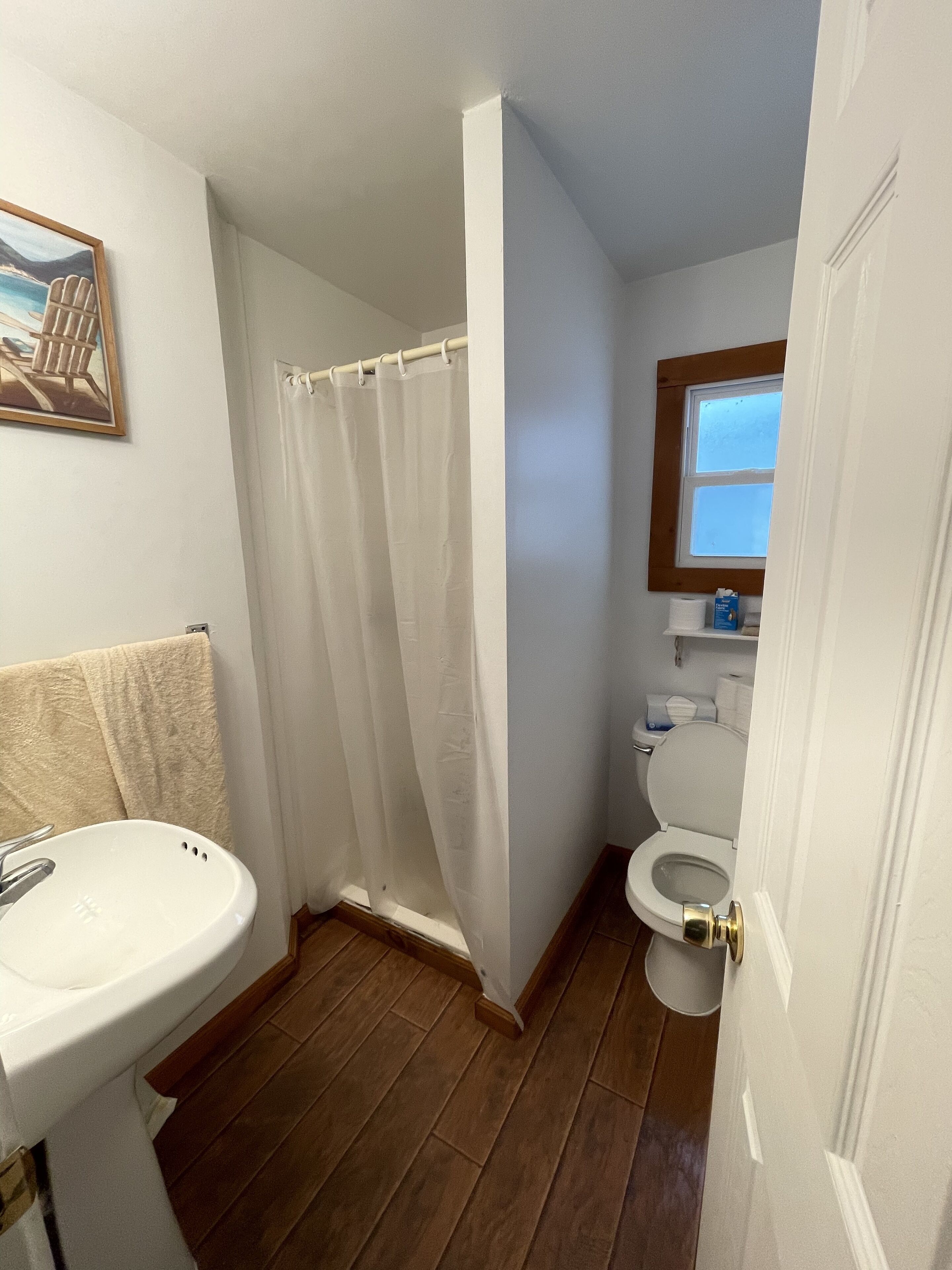 A bathroom with a wooden floor, a white sink, a toilet, and a shower curtain.