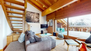 A modern interior with a wooden staircase, a sofa, a TV, and a view of a snowy landscape. - Terrasses du Paradis 7A LUXE & CENTER apart 7 pers (Haute-Nendaz)