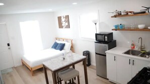 A compact room with a bed, a small table, a kitchenette, and a window. - Small Studio - Trinity Groves - 5 Min Downtown (Dallas)