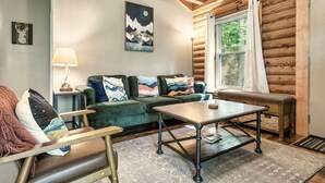 Ein gemütliches Blockhaus-Interieur mit einem grünen Sofa, einem Holztisch und einem großen Fenster mit Vorhängen.