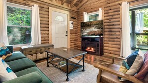 Ein gemütliches Blockhaus-Interieur mit Kamin, einer Couch, einem Tisch und großen Fenstern.