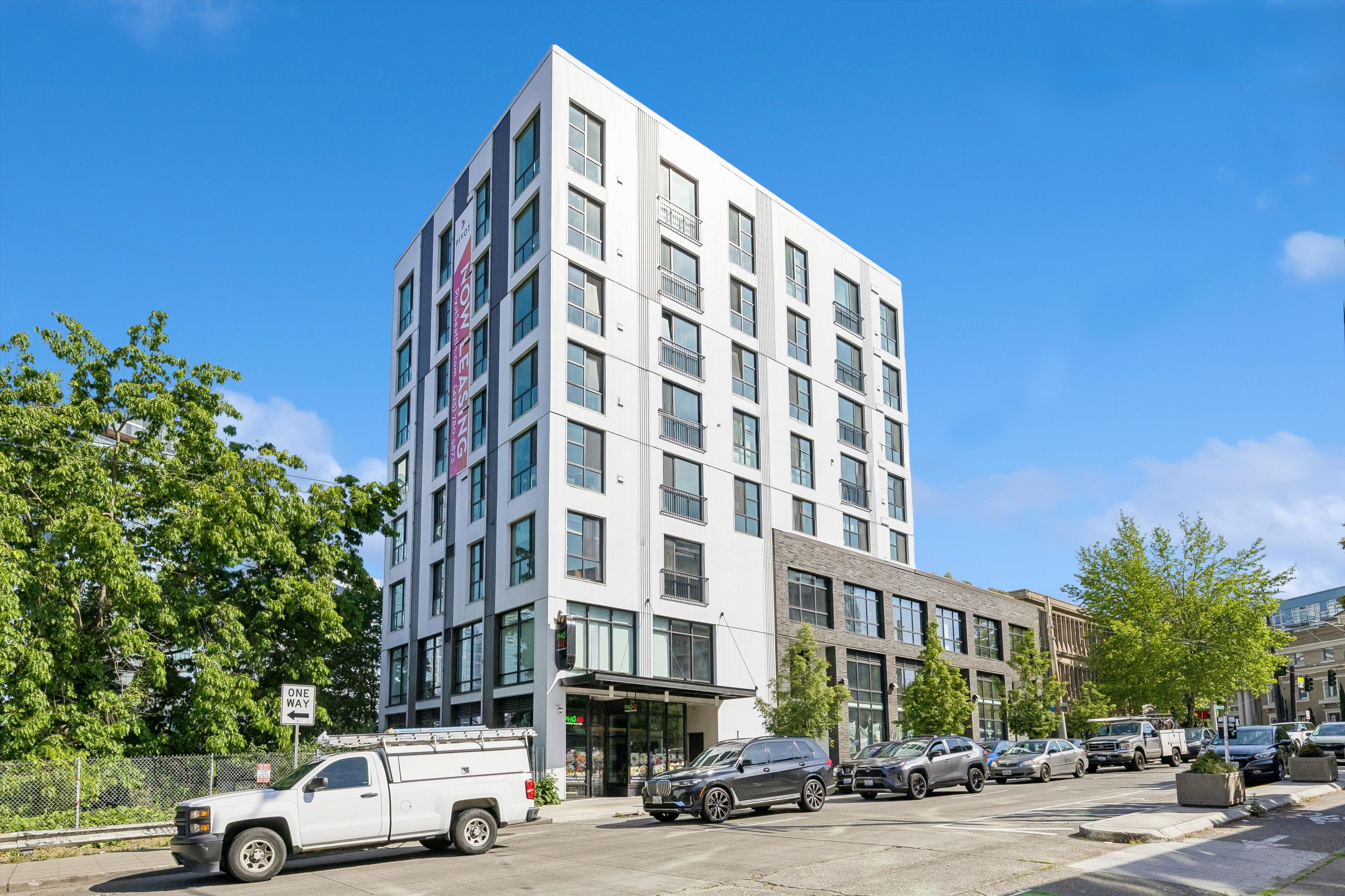 A multi-story hotel with a modern design, featuring a prominent entrance and a parking area with several vehicles.