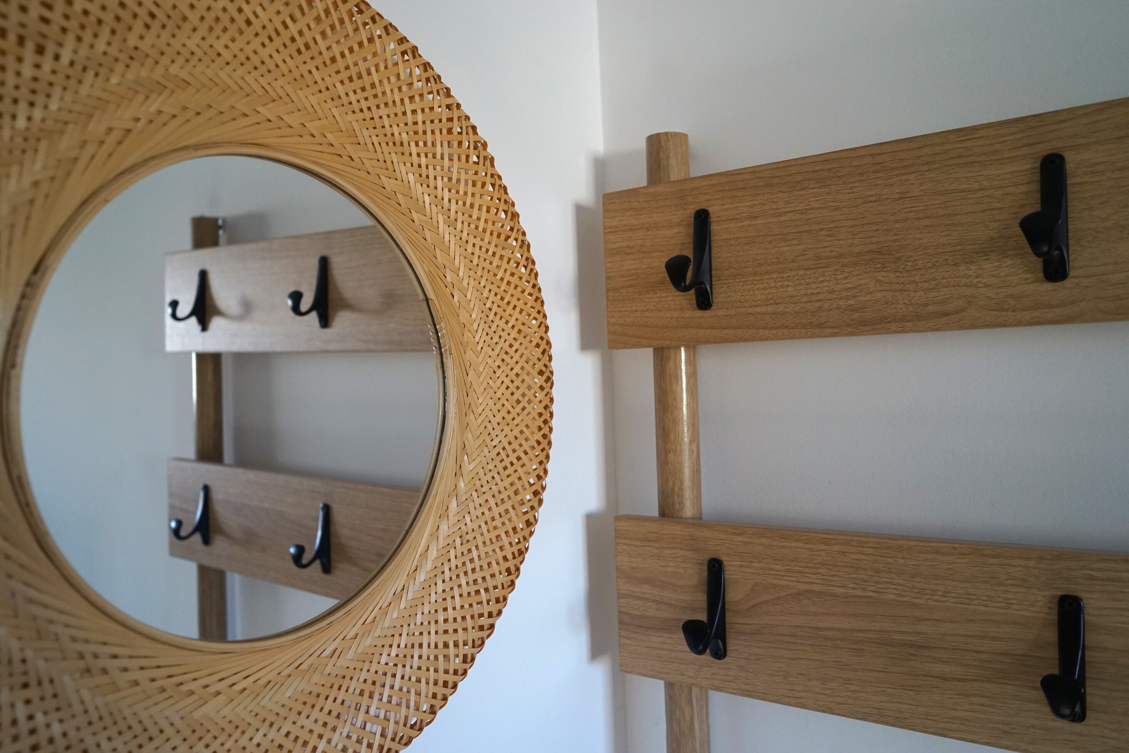 A wall-mounted wooden rack with hooks, a woven circular mirror, and a wooden beam.
