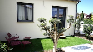 A modern house with a neatly trimmed lawn, a patio with red metal chairs, and a small tree. - Cosy new house in Provence, terrace (PIOLENC)