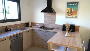 A modern kitchen with a dishwasher, sink, and a wooden dining table with chairs. - Cosy new house in Provence, terrace (PIOLENC)