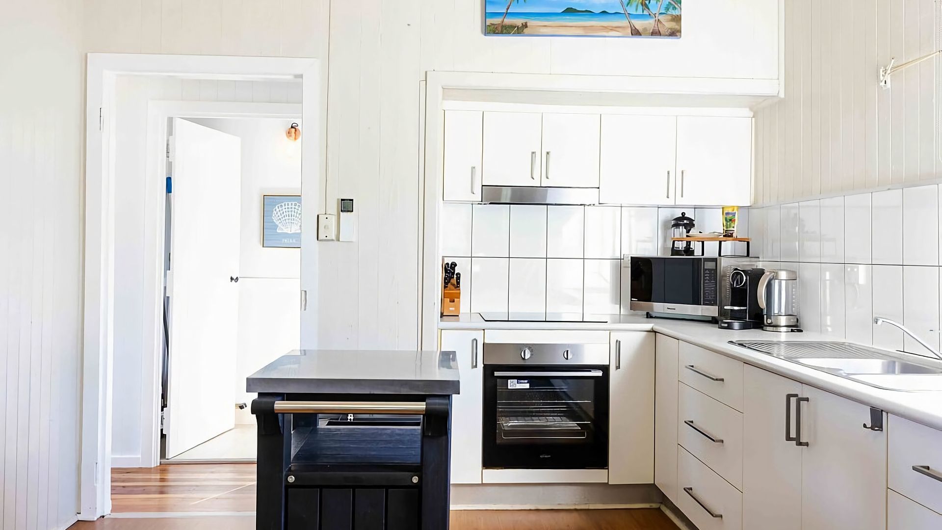 A modern kitchen with white cabinetry, a built-in oven, a microwave, and a coffee maker.