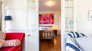 Habitació d'hotel amb un llit, un sofà vermell, un terra de fusta i una paret amb una pintura floral.