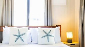 Ein Hotelzimmer mit einem Bett, zwei Kissen mit Sternfisch-Motiven, einem Nachttisch mit Lampe und Vorhängen.