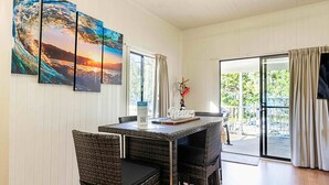 Uma área de refeições com mesa e cadeiras, um quadro na parede e vista pela porta de vidro.