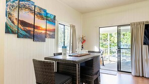 A dining area with a table and chairs, a painting on the wall, and a view through the glass door.