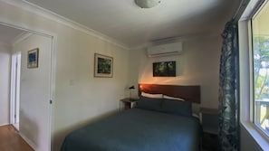 Ein Schlafzimmer mit einem Bett, einem Nachttisch, einer Klimaanlage und einem Fenster mit Vorhängen.
