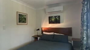 A bedroom with a bed, a nightstand, an air conditioning unit, and two framed pictures on the wall. - Mission Dreaming - 1 Bedroom Cottage (South Mission Beach)