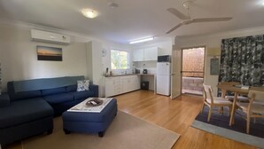 A living room with a sofa, ottoman, and a dining area with chairs and a table. - Mission Dreaming - 1 Bedroom Cottage (South Mission Beach)
